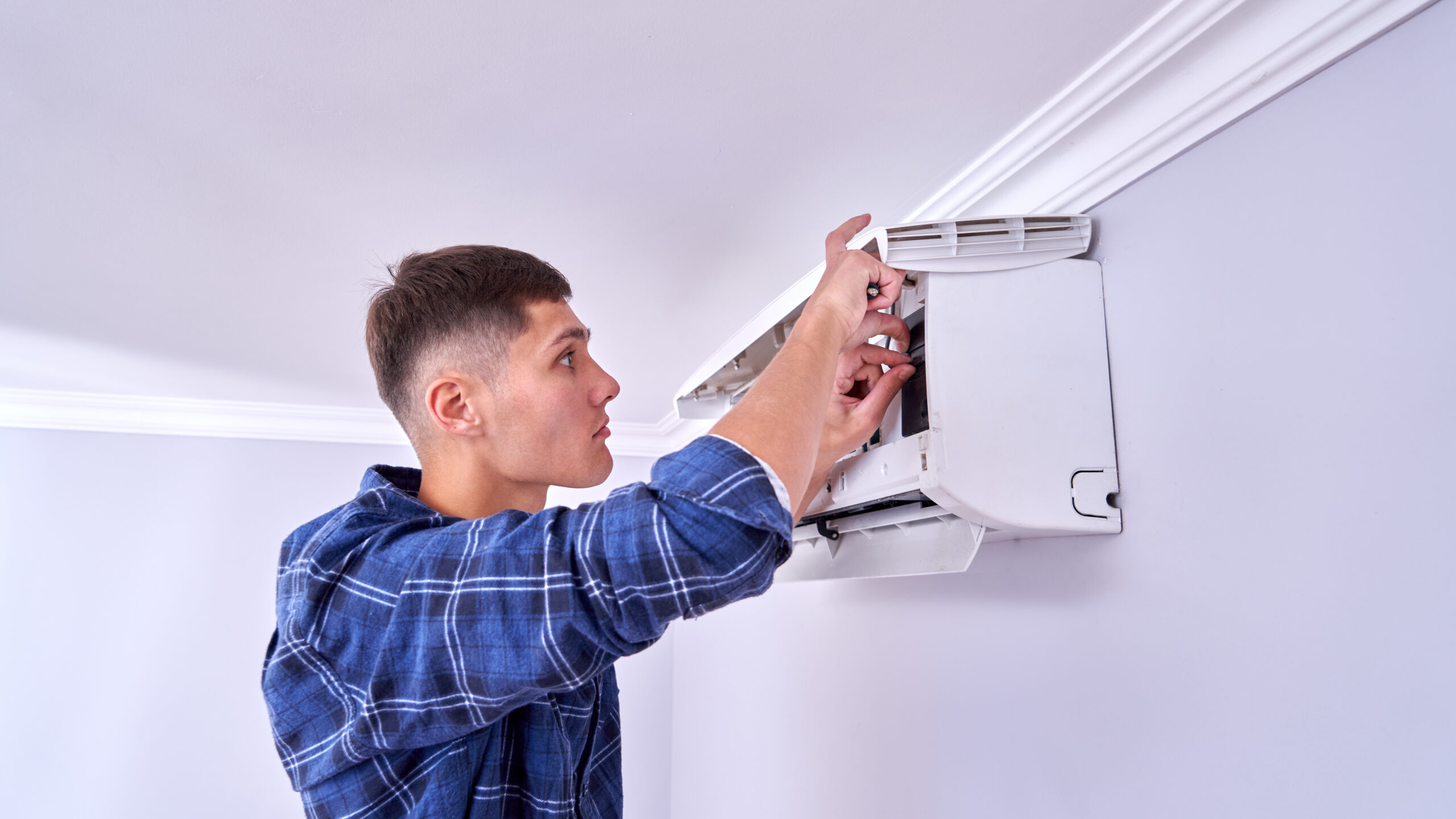 Caucasian male master in blue shirt cleans filters, installs and fixes air conditioner indoors